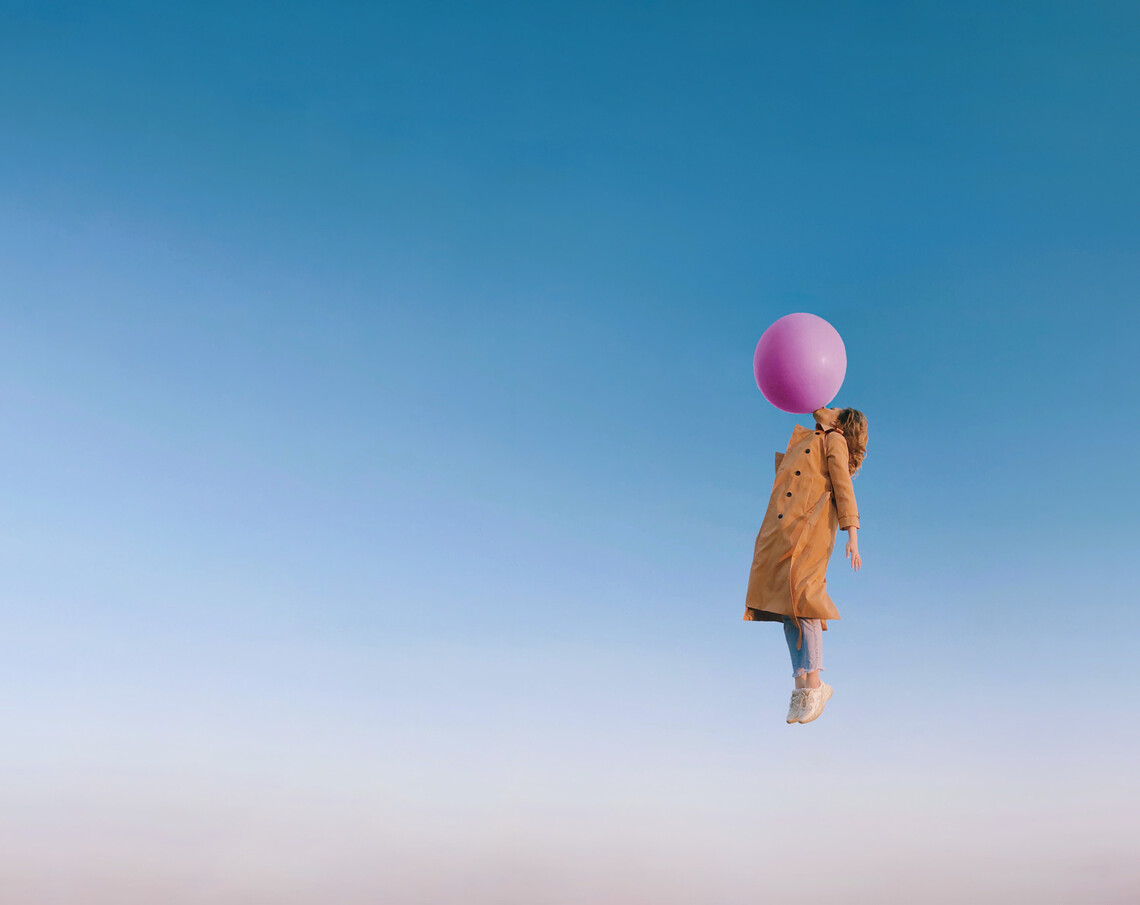 Eine Frau schwebt mit Luftballon am Himmel - Symbol für Leichtigkeit und ein Mindset der Gelassenheit